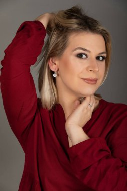 Gri arka planda kameraya bakan genç sarışın bir kadının portresi.   