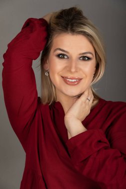 Gri arka planda kameraya bakan genç sarışın bir kadının portresi.   