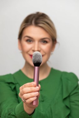 Genç ve güzel bir kadın makyajını fırçayla yapıyor.