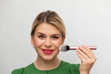 Genç ve güzel bir kadın makyajını fırçayla yapıyor.