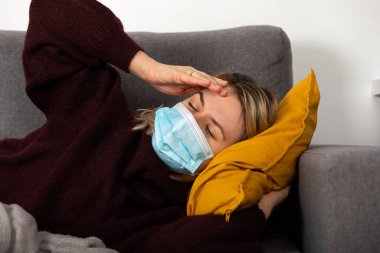 Coronavirus hastası genç bir kadın baş ağrısı ve ateşi var, kanepeye kıvrılmış bir şekilde yatıyor.