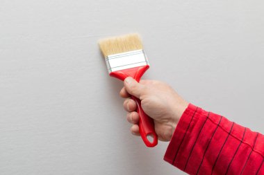 Beyaz arka planda kırmızı boya fırçası tutan bir adam.