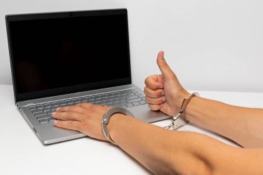 Gri bir dizüstü bilgisayarın önünde elleri kelepçeli.