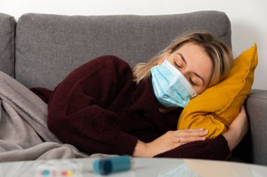 Coronavirus hastası genç bir kadın baş ağrısı ve ateşi var, kanepeye kıvrılmış bir şekilde yatıyor.