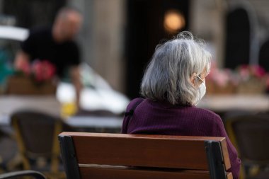 Bankta oturan yaşlı bir kadının fotoğrafı.