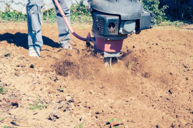 Çiftçi, kırsal kesimde güneşli bir bahar gününde modern mekanik döner dümeniyle toprağı sürüyor.