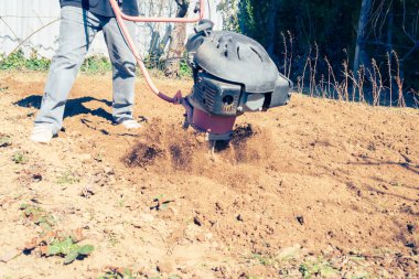 Çiftçi, kırsal kesimde güneşli bir bahar gününde modern mekanik döner dümeniyle toprağı sürüyor.
