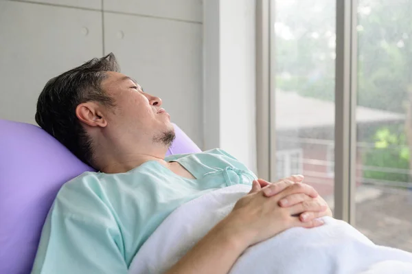 Asian patient man lying in hospital bed and looking at distance