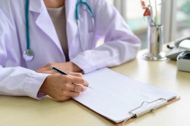 Close-up of doctor sitting at table and making notes in medical record