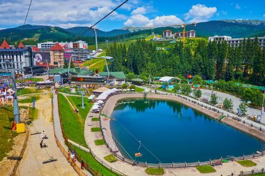 BUKOVEL, UKRAINE - 25 Temmuz 2021: Kayak asansörü 25 Temmuz 'da Bukovel Dağı eteklerinde yer alan Trout Pond, turist kafeleri ve otellerde gezinti yapar.