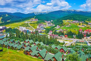 Teleferik, Bukovel tatil köyünün modern çatı, kır evi ve otellerini, Karpat dağlarının yeşil yamaçlarını ve parlak mavi gökyüzünü, Ukrayna 'yı izliyor.