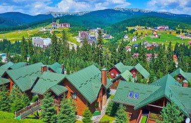 Bukovel dağ beldesinin manzarası, ön planda turist kulübelerinin modern yeşil çatısına sahip teleferik vagonundan, Karpatlar, Ukrayna