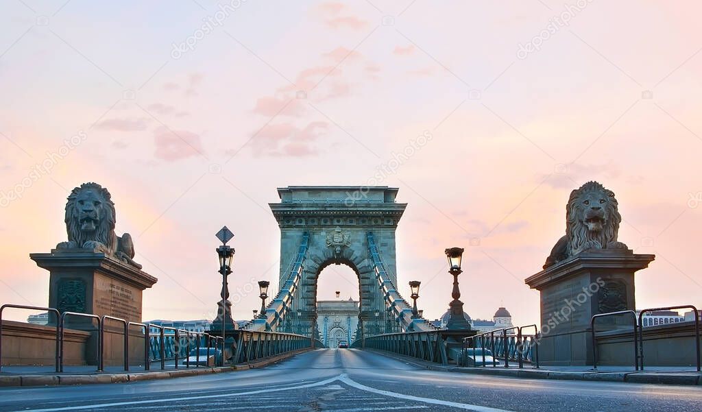 The scenic historic Chain Bridge with carved stone arches, vintage streetlights and lion sculptures against the dawn sky, Budapest, Hungary