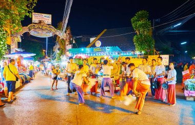 Chiang Mai, Tayland - 4 Mayıs 2019: Müzisyenler Wualai yürüyüş sokağındaki Cumartesi Gecesi Marketinde 4 Mayıs 'ta Chiang Mai' de bateri çalarken, iki genç sanatçı ritüel savaş dansı yaptılar.