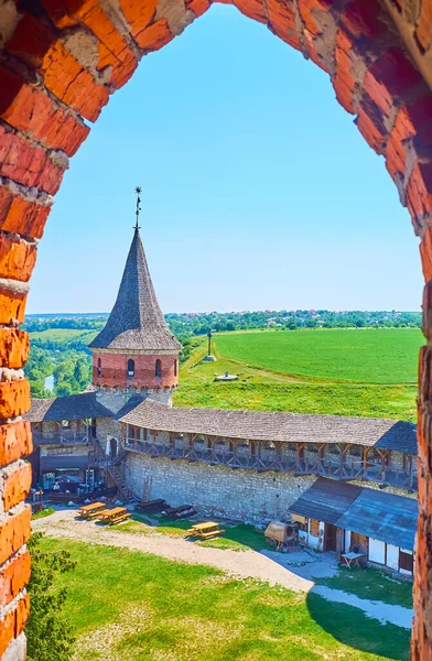 Kamianets-Podilskyi Kalesi 'nin eski kulesinin açığı arka plandaki parlak yeşil alanlara karşı Laska Kulesi' nin avlusunu, surlarını ve konisini gözlüyor.