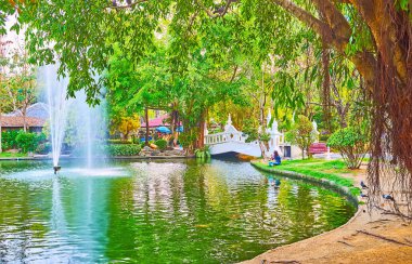 Banyan ağacının hava kökleri, yeşil çimenler ve Buak Hard halk parkındaki çeşmenin çevresindeki yemyeşil tropik yeşillik, Chiang Mai, Tayland
