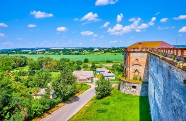 Medzhybizh Kalesi 'nin devasa ortaçağ duvarı ve tuğla yan kulesi, tarım arazileri ve evlerle çevrili, Ukrayna