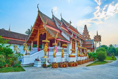 Wat Puak Hom Tapınağı 'nın manzaralı yeşil zemininde süslü Viharn' ı, Buda ve keşişlerin altın heykelleriyle çevrili, Chiang Mai, Tayland