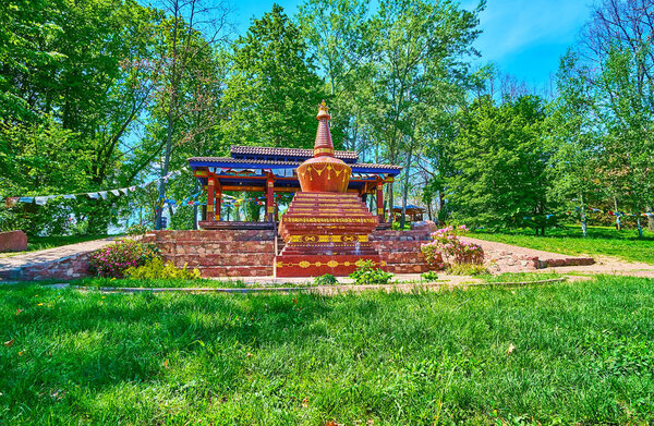 Relax on the lawn of Tibetan Garden with a view on the red chorten, decorated with gilt patterns and inscriptions, Kyiv Botanical Garden, Ukraine
