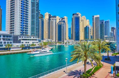Dubai Marina şehrinin modern beyaz yatı, gelecekteki gökdelenler ve bereketli palmiye ağaçları boyunca yüzüyor, Dubai, BAE
