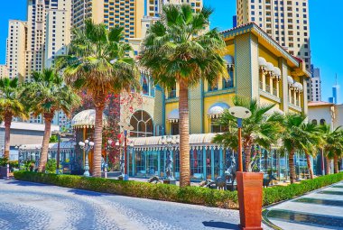 Bereketli palmiye ağaçları, Al Mamsha caddesindeki JBR Marina Plaj Bölgesi, Dubai, BAE 'deki lüks restoranın eski tarz malikanesini gizliyor.