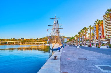 Malaga Limanı manzaralı, yelkenli, yatlı, yüksek palmiyeli, modern binalı ve arka planda yeşil tepeli Muelle Uno gezintinin tadını çıkarın.