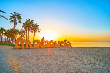 Malaga, İspanya - 29 Eylül 2019: 29 Eylül 'de Malagueta sahilinde güzel bir tabela, palmiyeler ve sakin Akdeniz sularıyla gün doğumunu izleyin