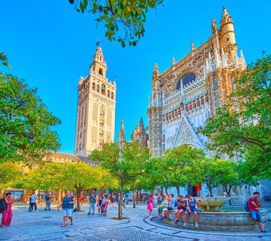 SEVILLE, SPAIN - 2 Ekim 2019: Seville Katedrali Orange Trees Garden 'daki ağaçların gölgesinde Giralda Kulesi manzaralı ve 2 Ekim' de Seville 'deki çeşmenin arkasındaki süslü Gotik Portal manzaralı rahatla