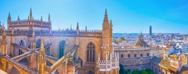 Ön planda Sevilla Katedrali 'nin Gotik çatısı ve ufukta modern Torre Sevilla gökdeleniyle Giralda çan kulesinin panoramik manzarasının tadını çıkarın.