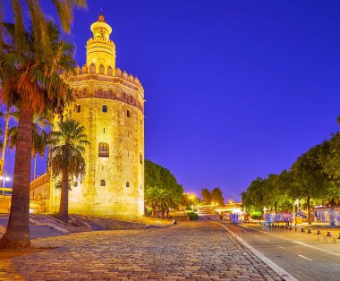 Akşam Cristobal Colon caddesi yemyeşil ağaçlar ve parlak aydınlatılmış tarihi Torre del Oro (Altın Kule), Seville, İspanya