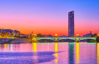 Guadalquivir Nehri üzerindeki sihirli mor alacakaranlık dalgalı yüzeyi parlak gökyüzünü, şehir binalarını ve ışıkları, Seville, İspanya 'yı yansıtıyor.