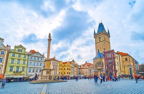 PRAGUE, CZECH REPUBLIC - MARCH 5, 2022: The Marian Column and clocktower of Old Town Hall, surrounded with colorful medieval houses of Old Town Square, on March 5 in Prague