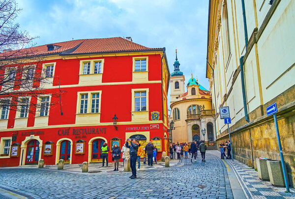 PRAGUE, CZECH REPUBLIC - MARCH 5, 2022: The bright red House at the Golden Snake (Dum u Zlateho Hada) with apse of St Clement Cathedral in background, Karlova Street, on March 5 in Prague
