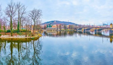 Vltava Nehri 'nin ayna suları, arka planda görülen Slavonic Adası, Petrin Tepesi' ndeki parkı ve Çek Cumhuriyeti 'nin Prag kentindeki kemerli taş Lejyon Köprüsü' nü yansıtır.