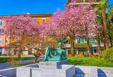 The statue fountain and blooming cherry trees in Parchetto Lanchetta Park of Lugano, Switzerland clipart
