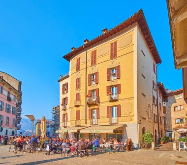 COMO, İtalya - 20 Mart 2022 Alessandro Volta Meydanı 'ndaki kalabalık açık hava restoranı arkasında parlak sarı tarihi bina manzaralı, 20 Mart' ta Como