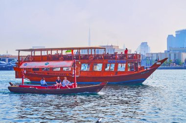 DUBAI, BAE - 1 Mart 2020: Geleneksel ahşap küçük abra tekne ve Dubai Creek 'te geniş dhow yolcu teknesi, arka planda Burj Halife' nin silüeti, 1 Mart 'ta Dubai' de