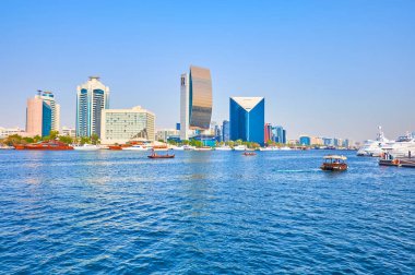 DUBAI, BAE - 1 Mart 2020 Dubai Creekin 'in dalgalı mavi suları Dubai Ulusal Bankası ve Ticaret Odası kuleleri ile modern Deira mimarisinin önünde 1 Mart' ta Dubai 'de