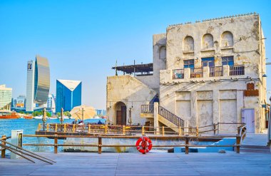 DUBAI, BAE - 1 Mart 2020: Dubai Port Saeed 'in Deira Port Saeed ilçesinin klasik kerpiç evi, Dubai Creek ve modern binaları manzaralı Al Seef mahallesinin bankası