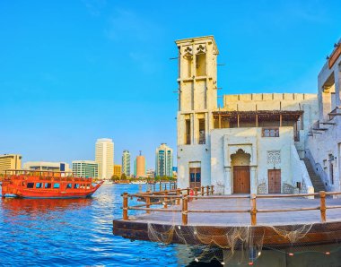 Klasik ahşap dhow teknesi Dubai Deresi boyunca Al Seef mahallesinin kıyısında üzerinde yalın rüzgar yakalayıcıları, Dubai, BAE ile kaplanmış geleneksel kerpiç evleri ile yüzüyor.