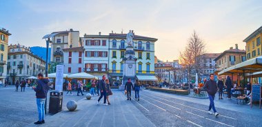 COMO, İtalya - 20 Mart 2022: Alessandro Volta Meydanı akşam panoraması Volta anıtı manzaralı eski binalar ve restoranların teraslarına karşı, 20 Mart 'ta Como' da