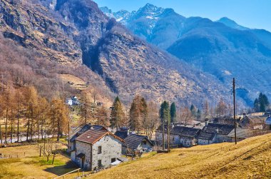 Verzasca Nehri boyunca uzun kozalaklı ağaçlarla Valle Verzasca manzarası, Lepontine Alpleri 'nin kayalık yamaçları ve İsviçre' nin Gerra kentinin küçük taş evleri.
