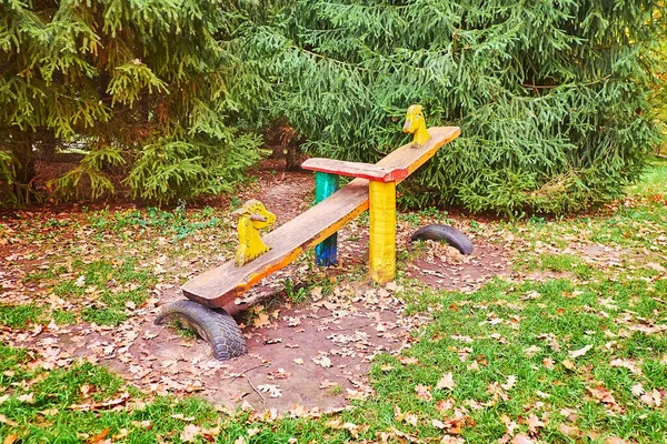 The handmade wooden teeter-totter with carved horse heads on kids playground, surrounded with spruces, Kyiv, Ukraine