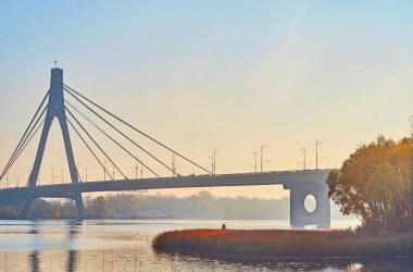 Enjoy the foggy autumn sunrise in Natalka Park on Dnieper River with hazy Pivnichnyi (Northern) Bridge in background, Kyiv, Ukraine