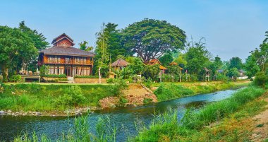 Panorama of Pai River, surrounded with tropical gardens, forests, tall grasses and wooden houses, Pai, Thailand