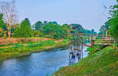 Pai river with rotating waterwheel and lush jungle on the opposite bank, Pai, Thailand