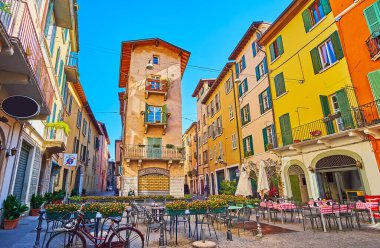 The small area with tables of outdoor restaurants, decorated with flowers in pots, surrounded with historic houses of  Vicolo due Torri street, Brescia, Italy