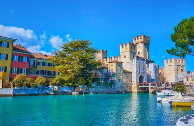 The small port of Sirmione tourist resort with a view on beautiful colored houses, hotels, Scaligero Castle and small boats, moored at the bank, Lombardy, Italy