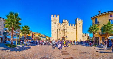 SIRMIONE, ITALY - APRIL 10, 2022: Panorama of The Piazza Castello square with outdoor restaurants and medieval Scaligero Castle with tall towers and massive ramparts, on April 10 in Sirmione