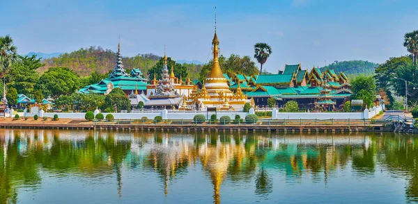 Panorama of the mirror surface of Nong Kham lake reflecting historic Wat Chong Kham and Wat Chong Klang temples, surrounded by lush greenery, Mae Hong Son, Thailand